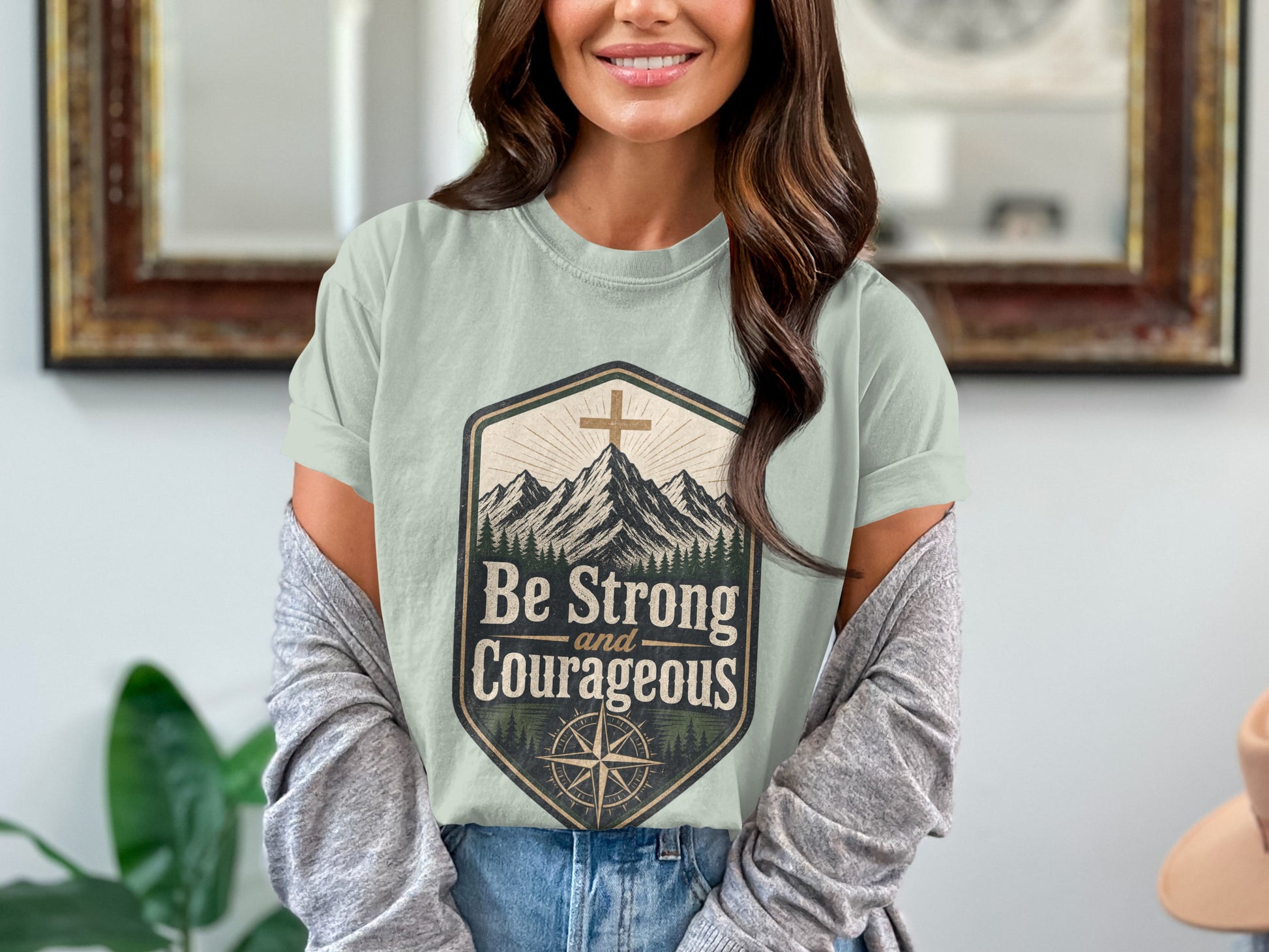 T-shirt graphic with mountains, cross, compass, and text "Be Strong and Courageous."