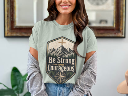 T-shirt graphic with mountains, cross, compass, and text "Be Strong and Courageous."