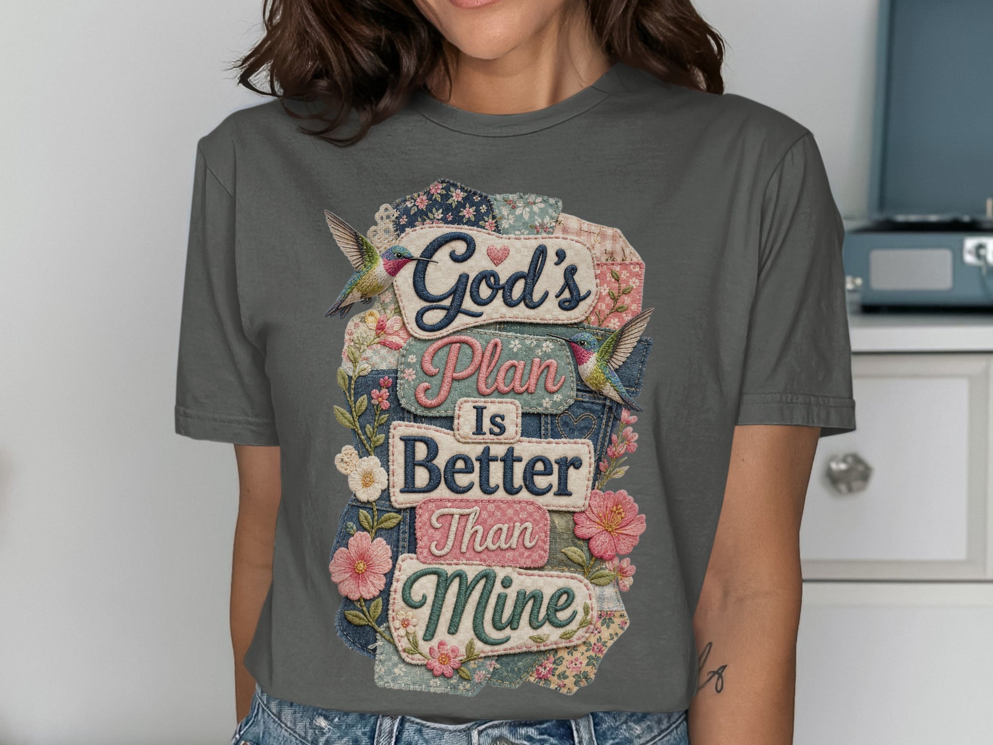 Gray t-shirt with "God's Plan Is Better Than Mine" text surrounded by floral patches and hummingbirds.