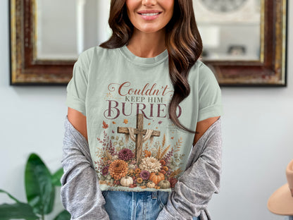 Light blue t-shirt with rustic cross and flowers graphic, reads "Couldn't Keep Him Buried."