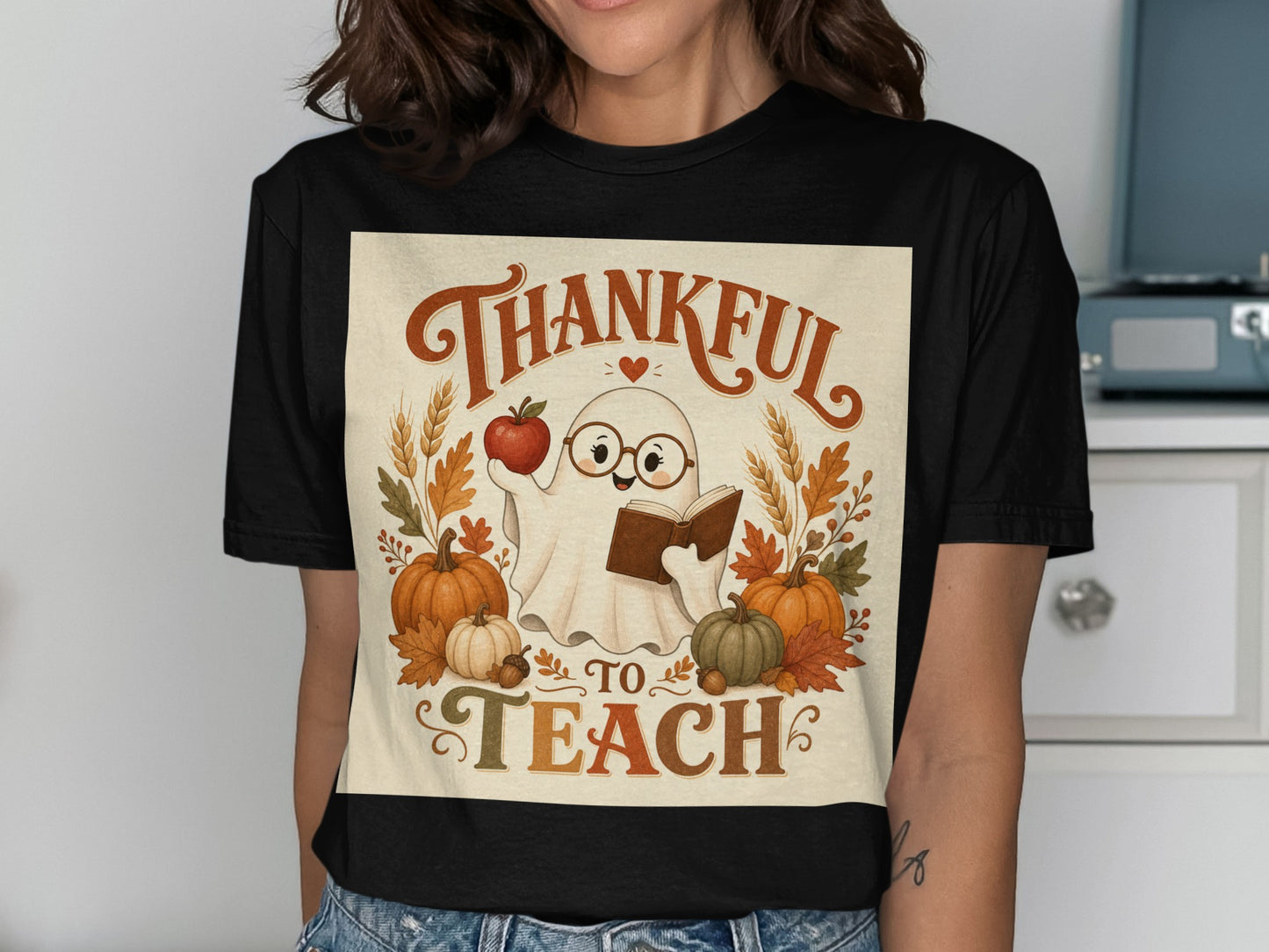 Ghost with glasses holding apple and book, surrounded by pumpkins and leaves, text says "Thankful To Teach".