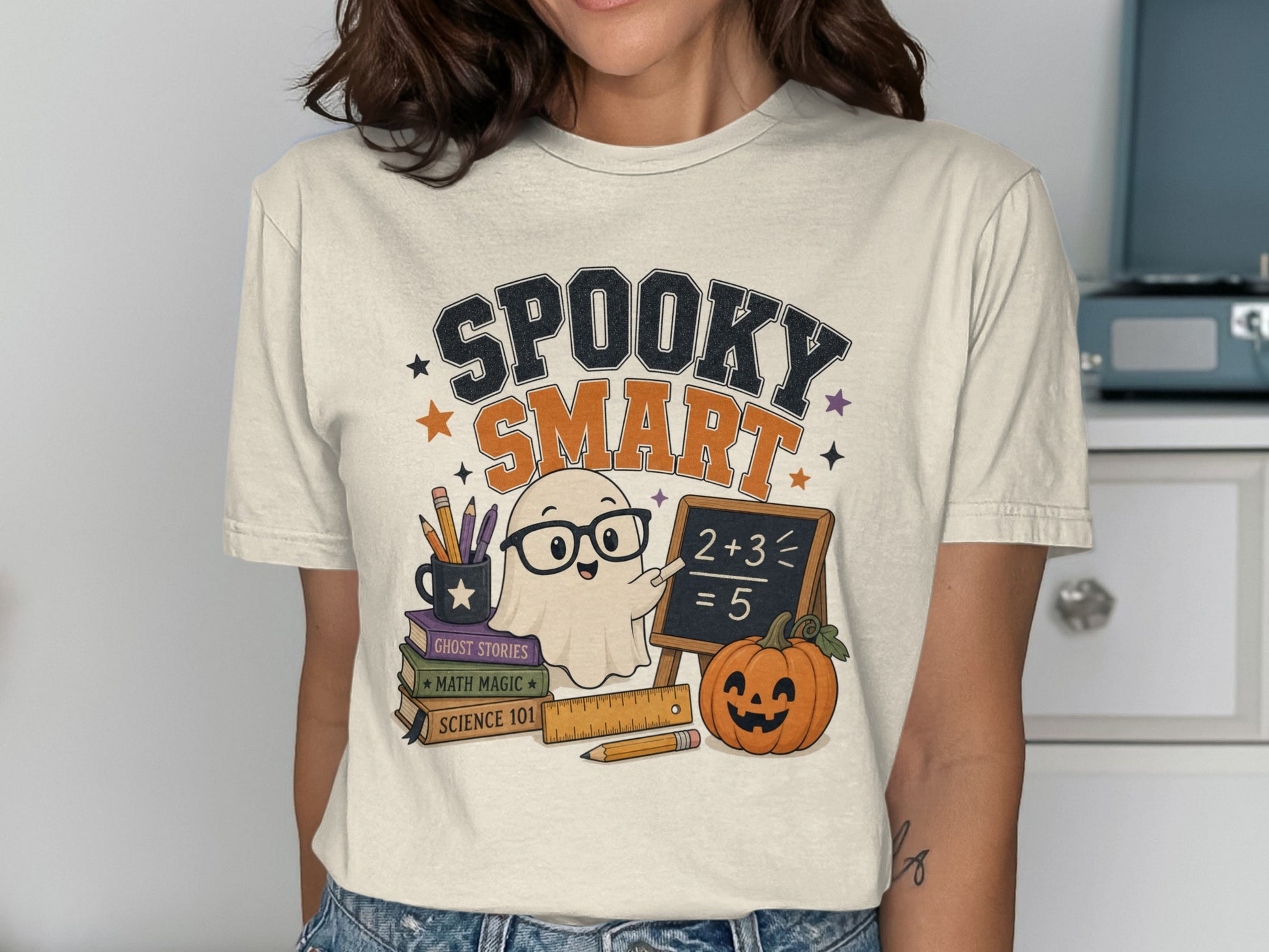 T-shirt graphic: "Spooky Smart" text, ghost with glasses teaching math, pumpkin, and books.