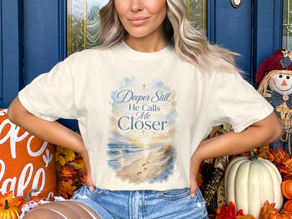 Cream t-shirt with beach sunset graphic and text "Deeper Still, He Calls Me Closer".