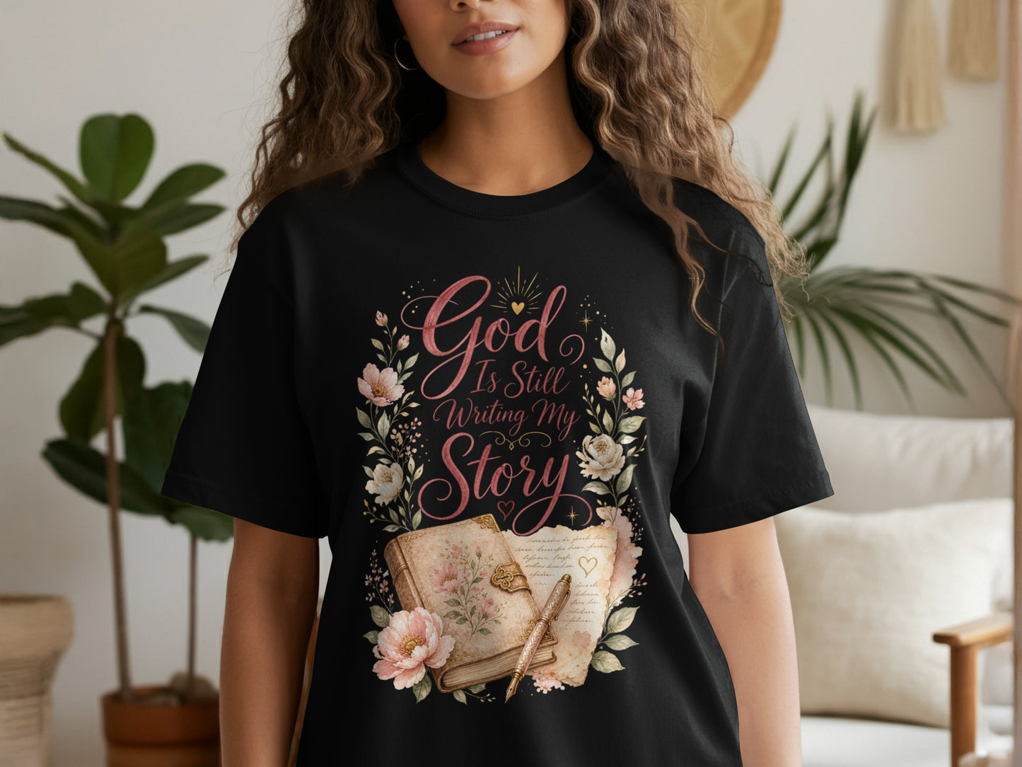 Black t-shirt with "God Is Still Writing My Story" graphic featuring floral wreath and open book.