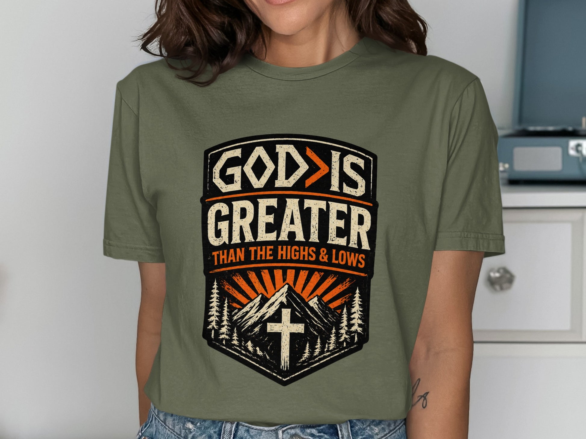 Green t-shirt with "GOD IS GREATER THAN THE HIGHS & LOWS" text and mountain graphic.