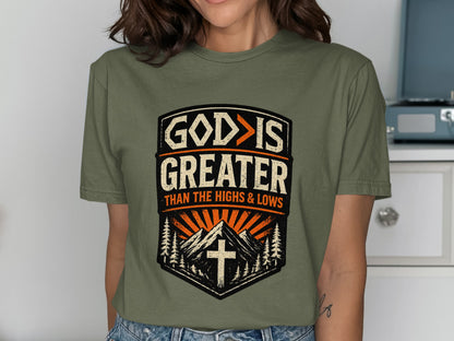 Green t-shirt with "GOD IS GREATER THAN THE HIGHS & LOWS" text and mountain graphic.