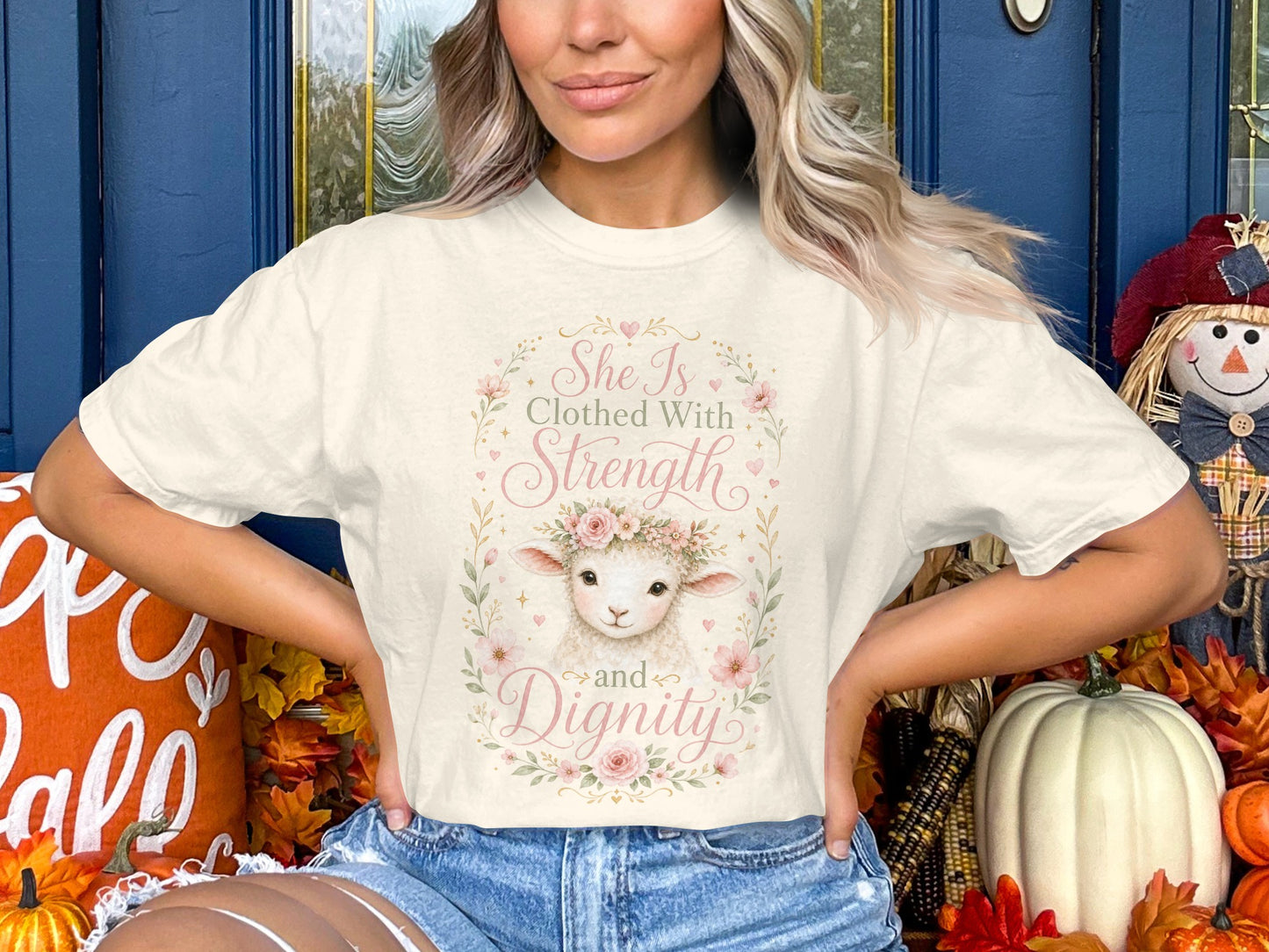 Cream t-shirt with a watercolor lamb wearing a floral crown and text "She Is Clothed With Strength and Dignity."