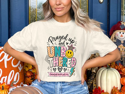Cream t-shirt with "Prayed up and UNBOTHERED because God's Got It" graphic.