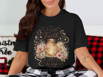 Black t-shirt featuring "A Little Faith Lights the Way" with a glowing jar and flowers.