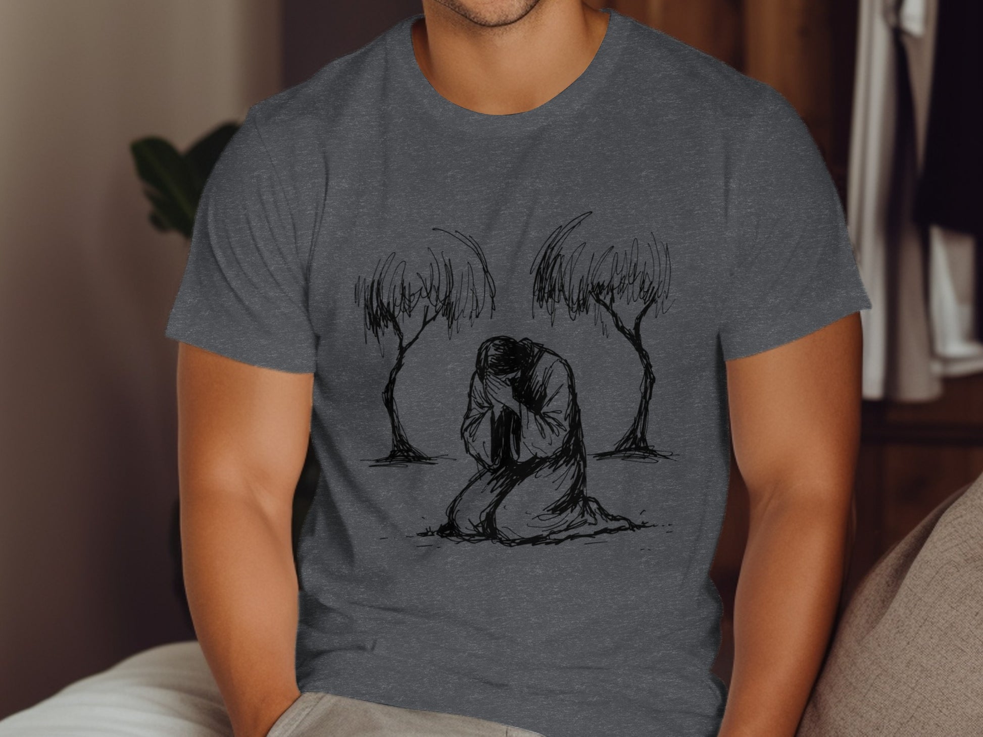 Man in charcoal t-shirt with line drawing of figure kneeling between two trees.