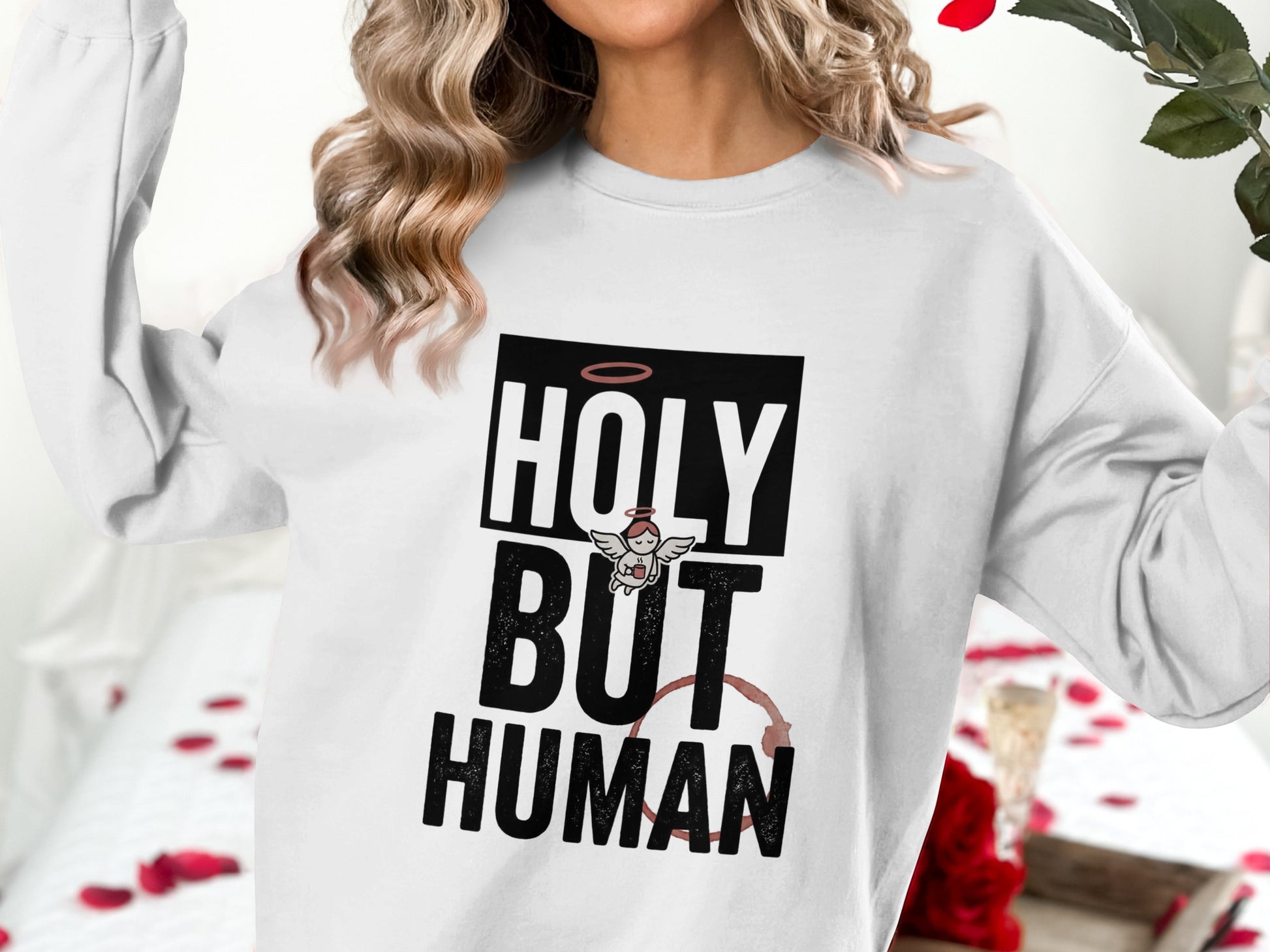 White sweatshirt with "HOLY BUT HUMAN" text and a small angel illustration.