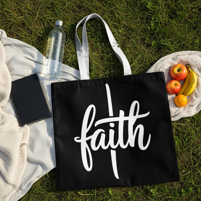 Black tote bag with white script lettering spelling "faith" on grass.