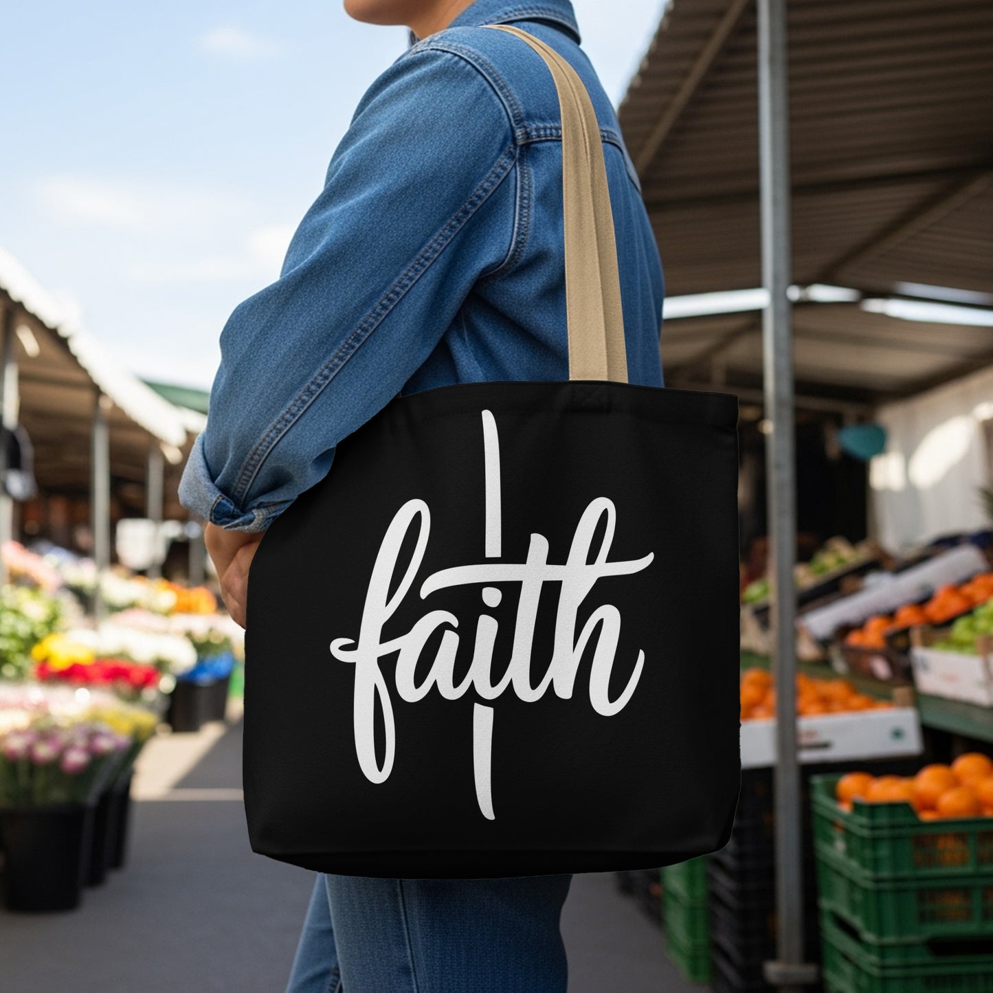 Black tote bag with white "faith" text held by a person in a denim jacket.