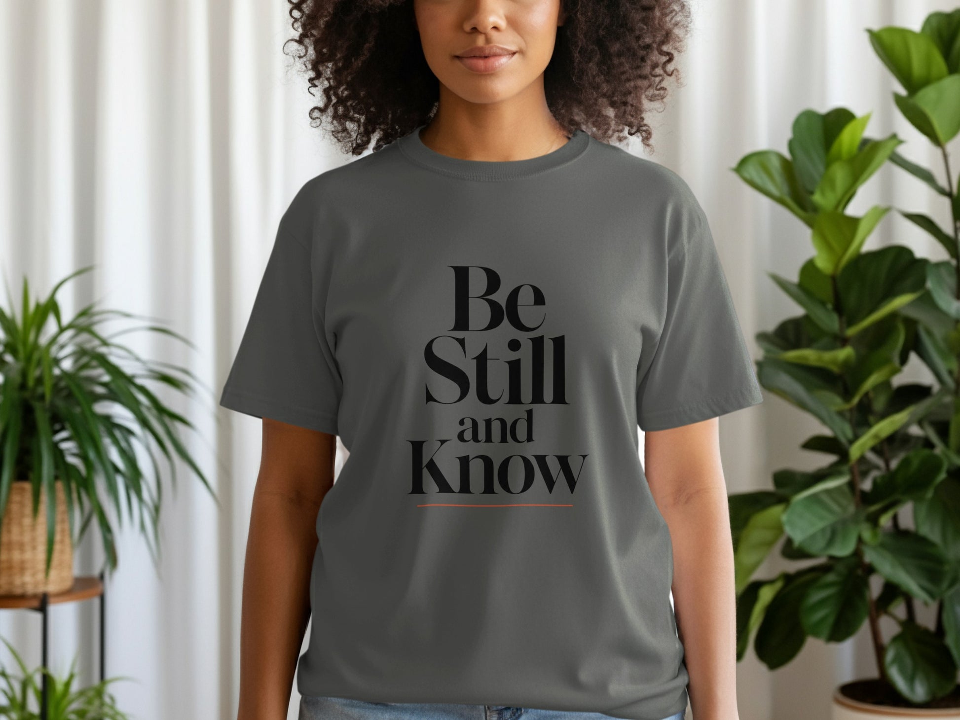 Grey t-shirt with "Be Still and Know" graphic and orange underline.