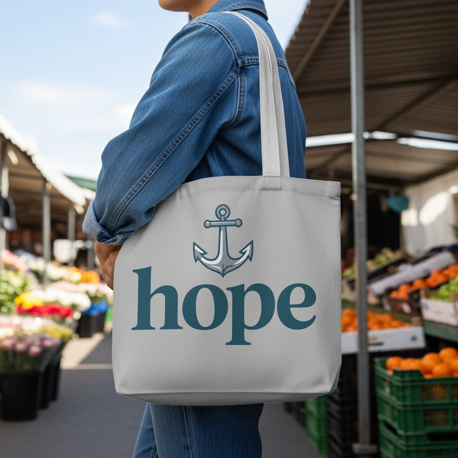 Grey tote bag with anchor icon and "hope" text, worn by person in denim jacket.