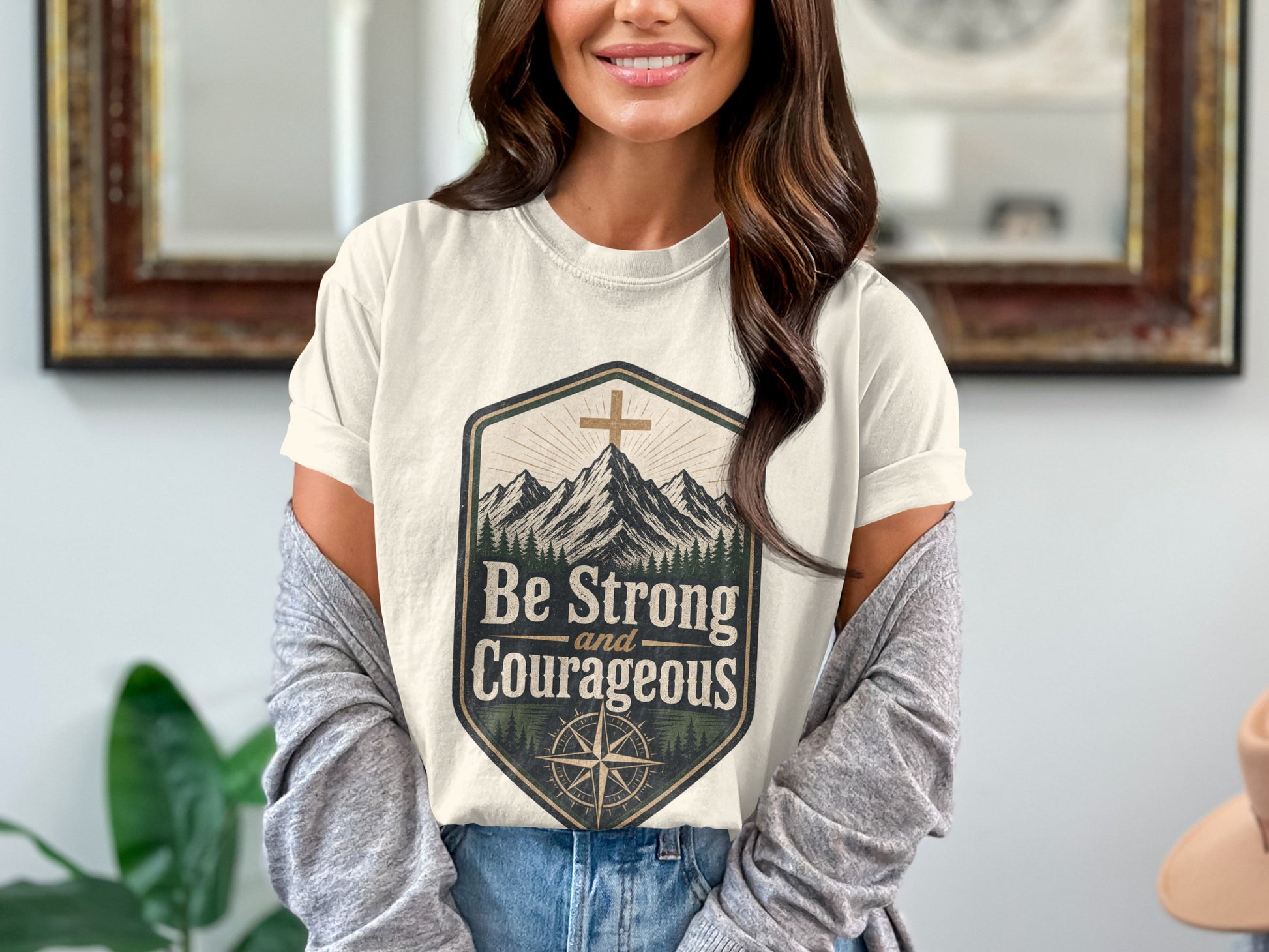 Cream t-shirt with mountains, cross, and "Be Strong and Courageous" text.