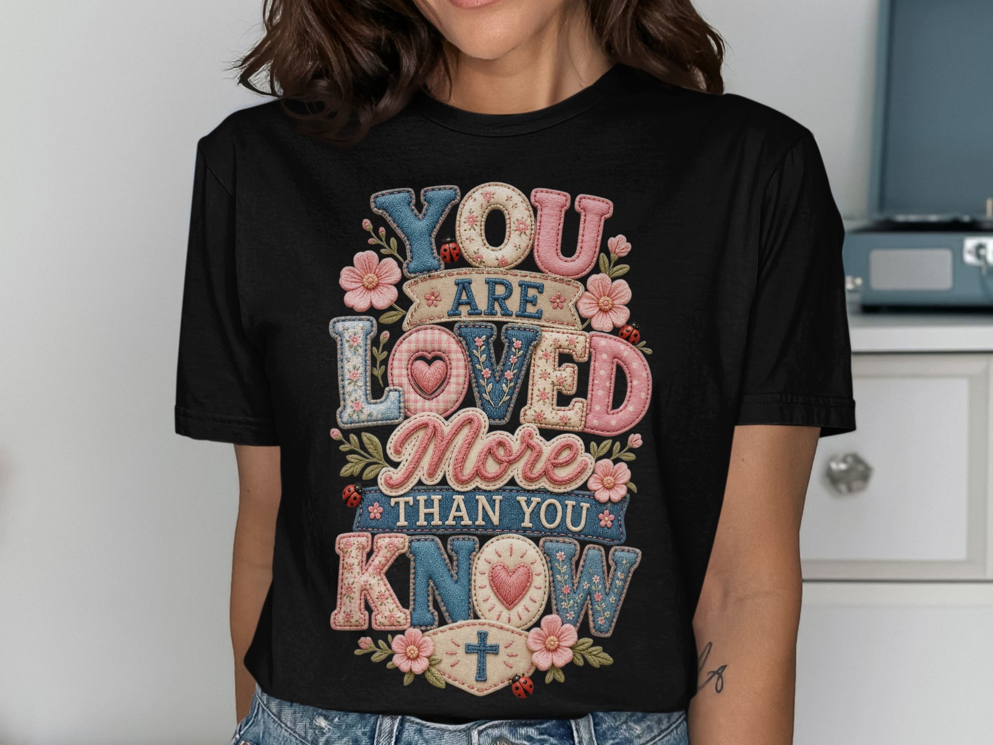 Black t-shirt with "YOU ARE LOVED MORE THAN YOU KNOW" floral embroidered text.