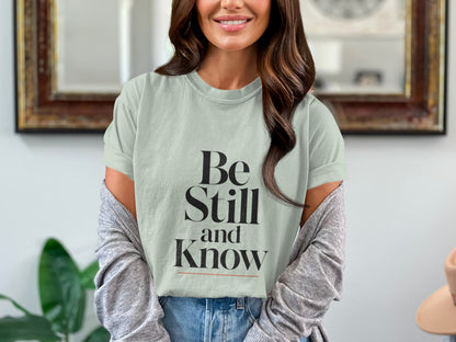 Light teal t-shirt with black text "Be Still and Know" and a peach hat.