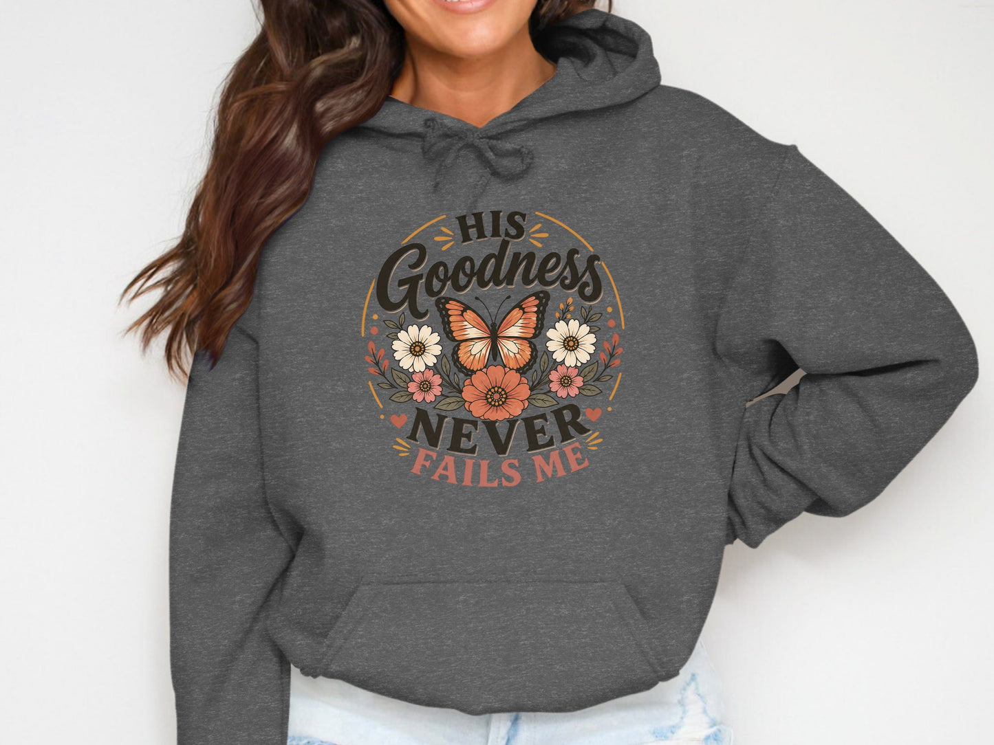 Dark grey hoodie with "His Goodness Never Fails Me" text and floral butterfly graphic.