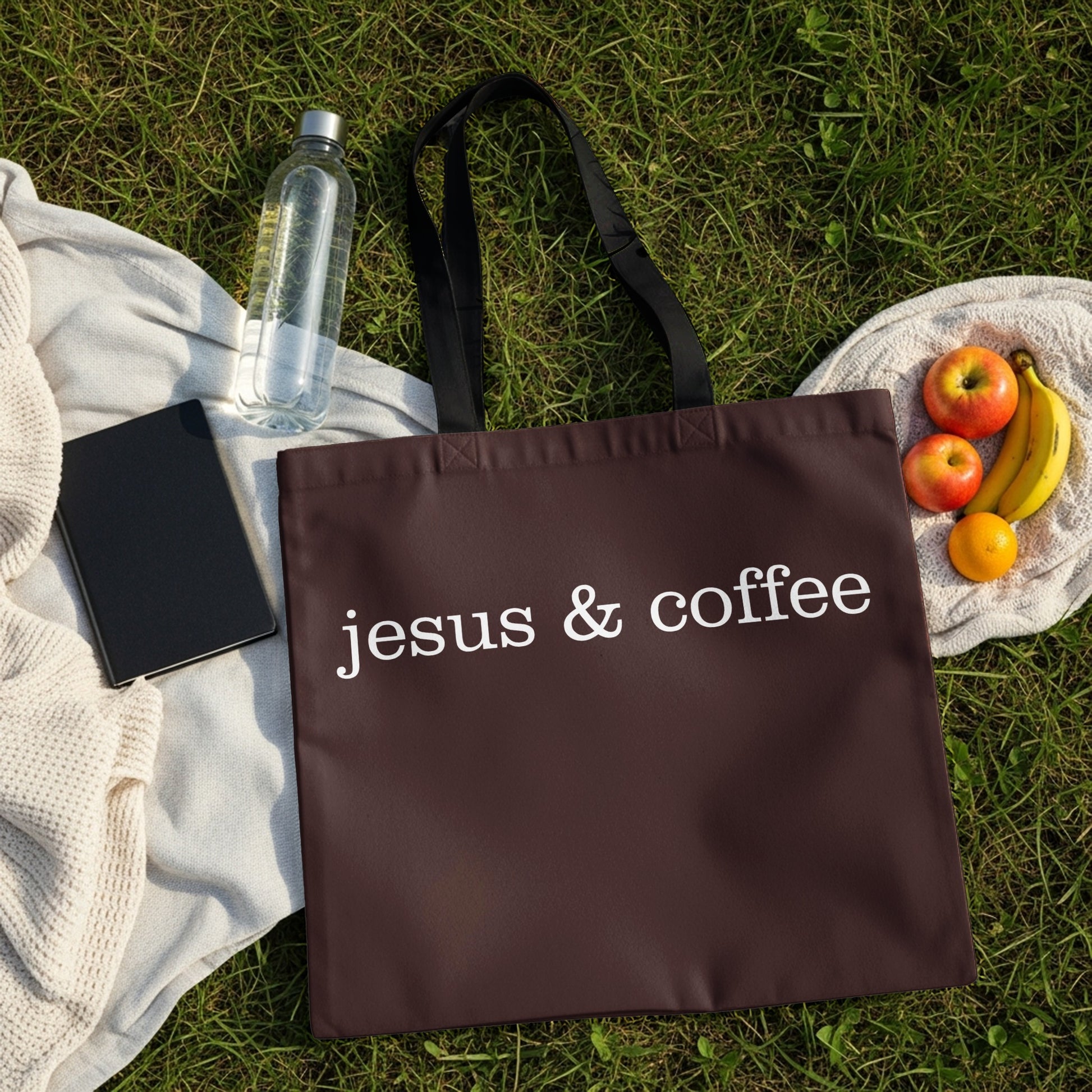 Brown tote bag with white text "jesus & coffee" on grass with fruit.
