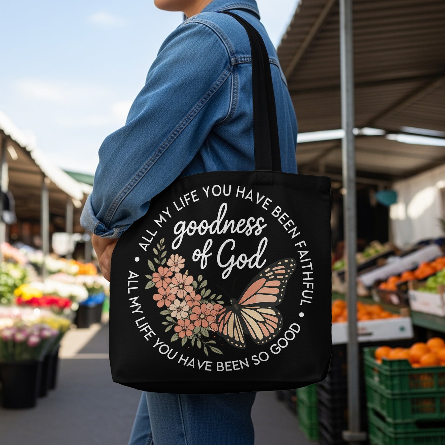 Black tote bag with a circular design of flowers, a butterfly, and text.
