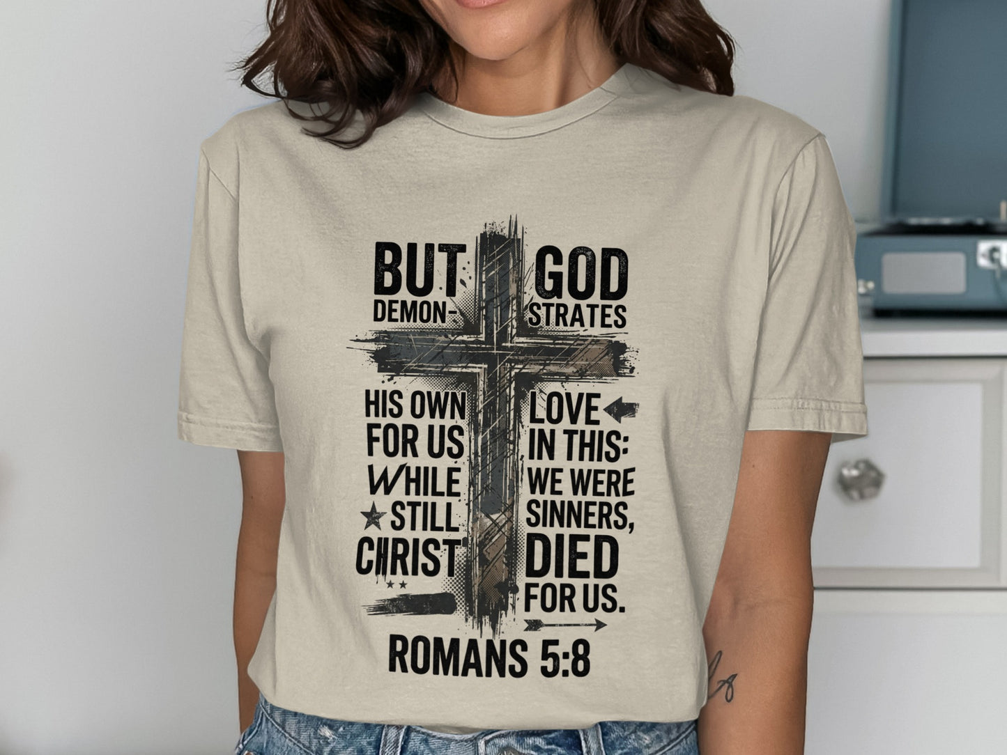 T-shirt with a cross graphic and religious text reading "But God Demonstrates His Own Love In This".