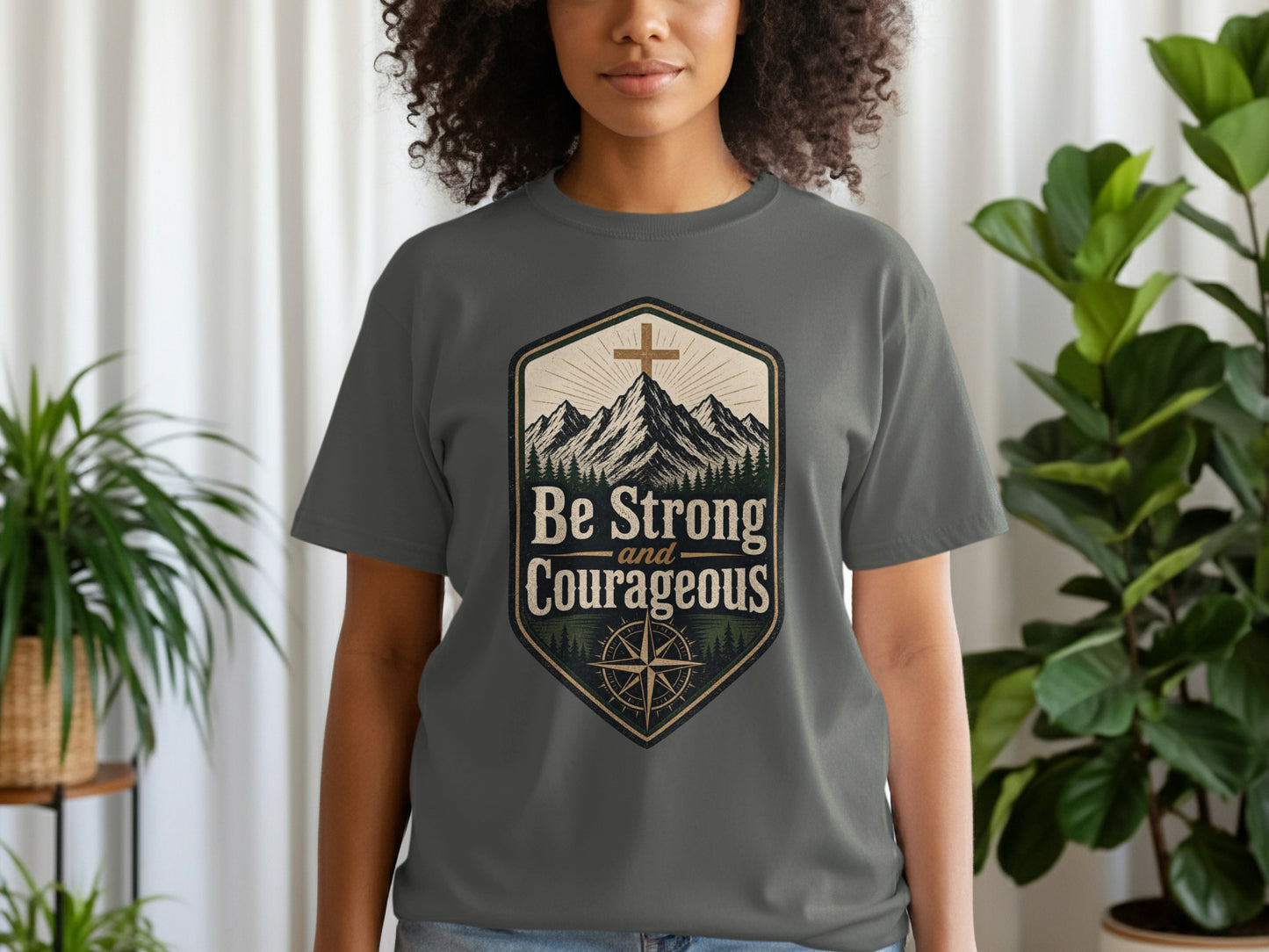 Grey t-shirt with a crest graphic featuring mountains, a cross, and the text "Be Strong and Courageous".