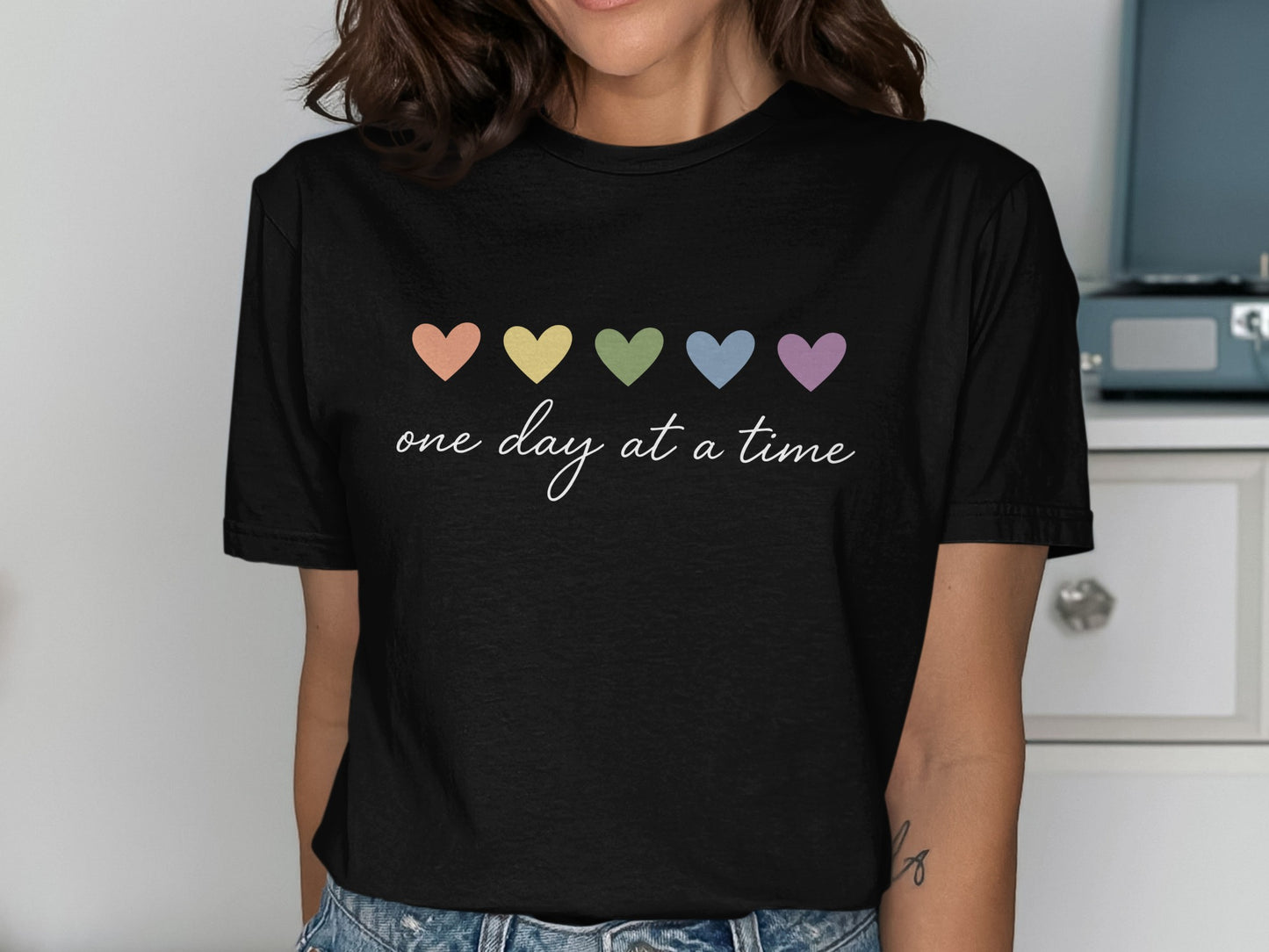 Black t-shirt with pastel heart shapes and "one day at a time" text.