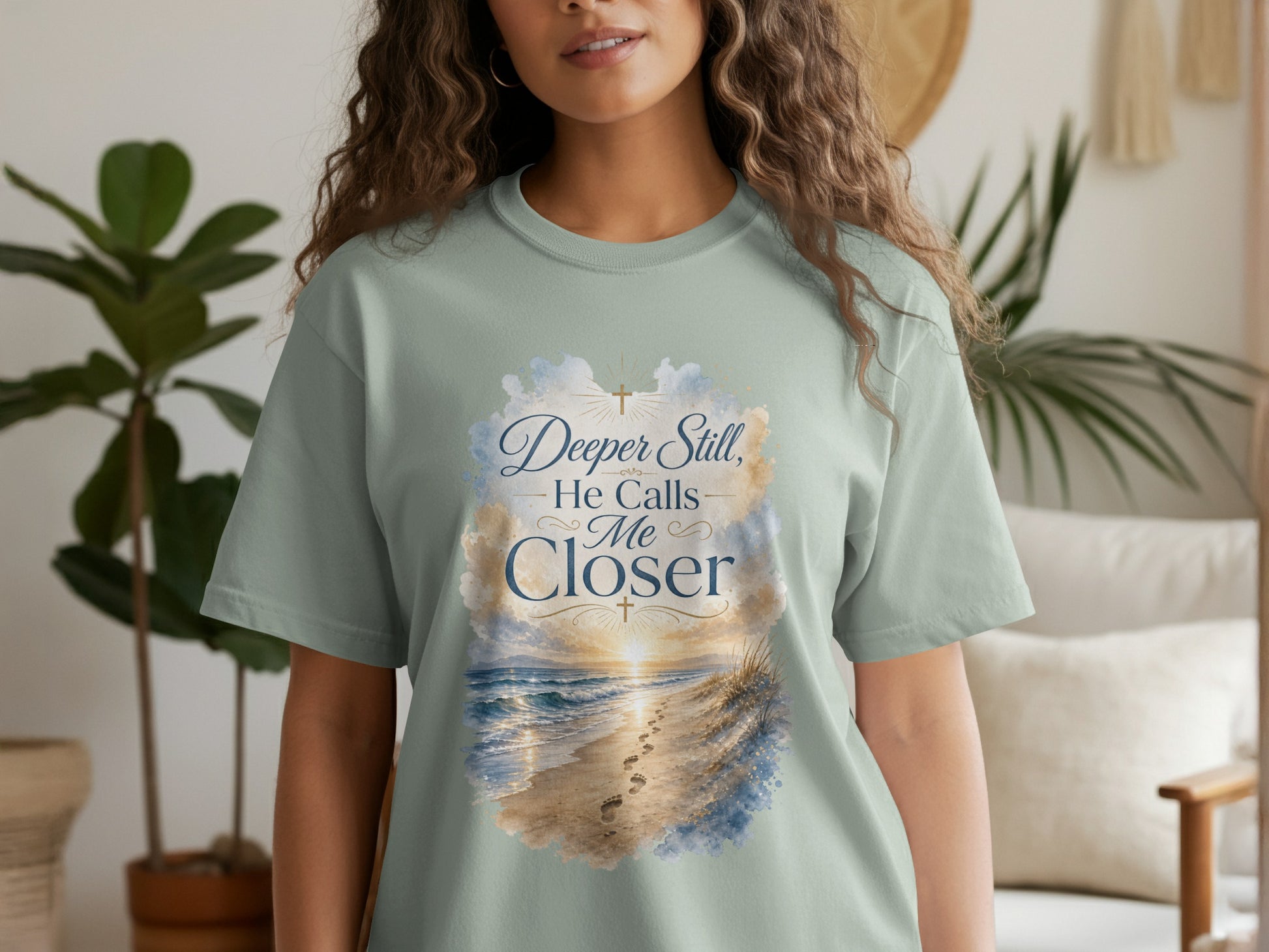Light green t-shirt with "Deeper Still, He Calls Me Closer" and beach sunset graphic.