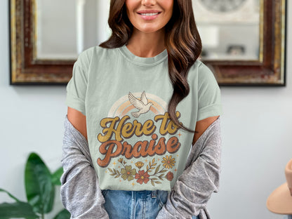 Light green t-shirt with "Here to Praise" text, dove, rainbow, and flowers graphic.