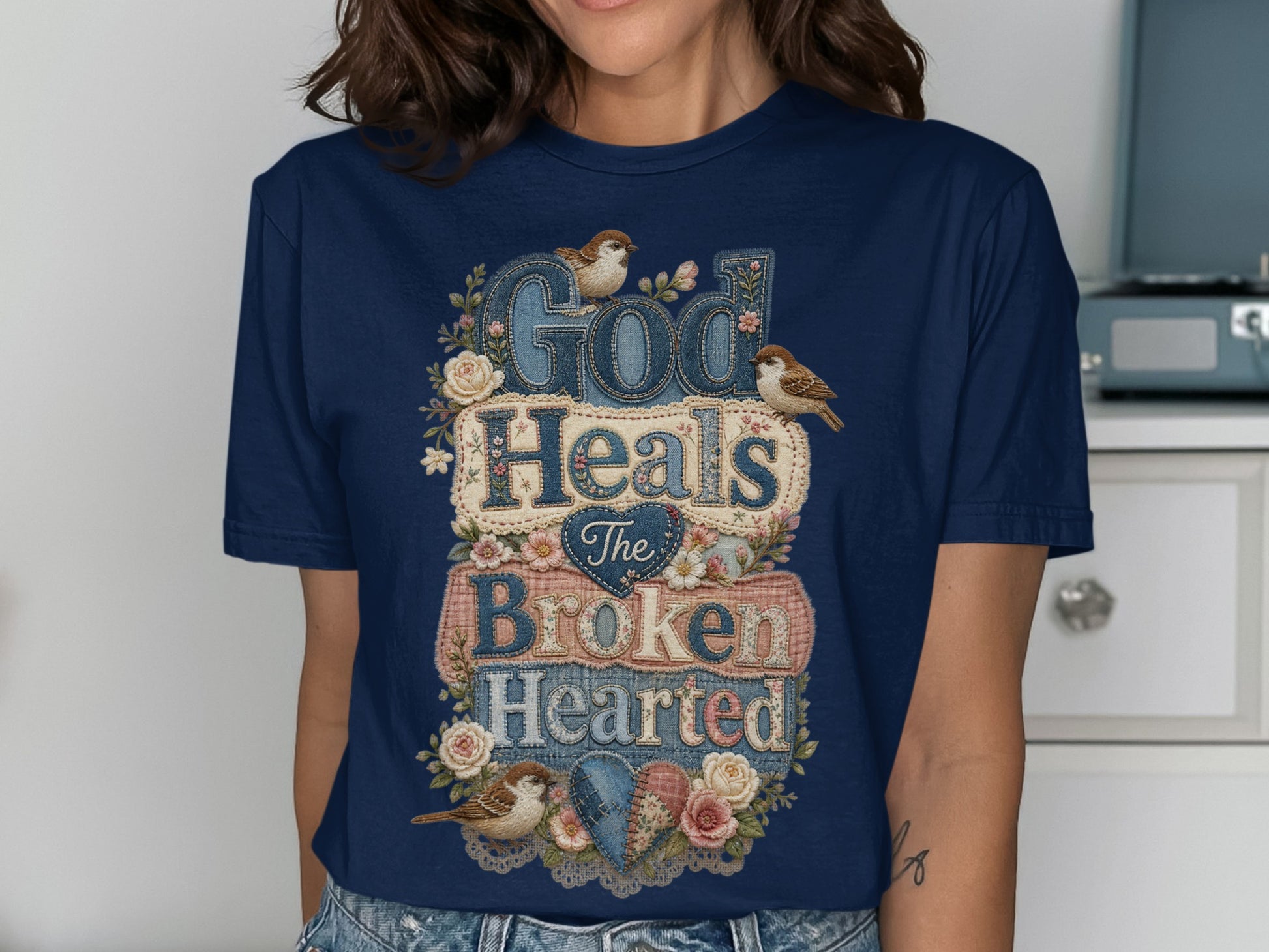 Dark blue t-shirt with "God Heals The Broken Hearted" text and floral accents.