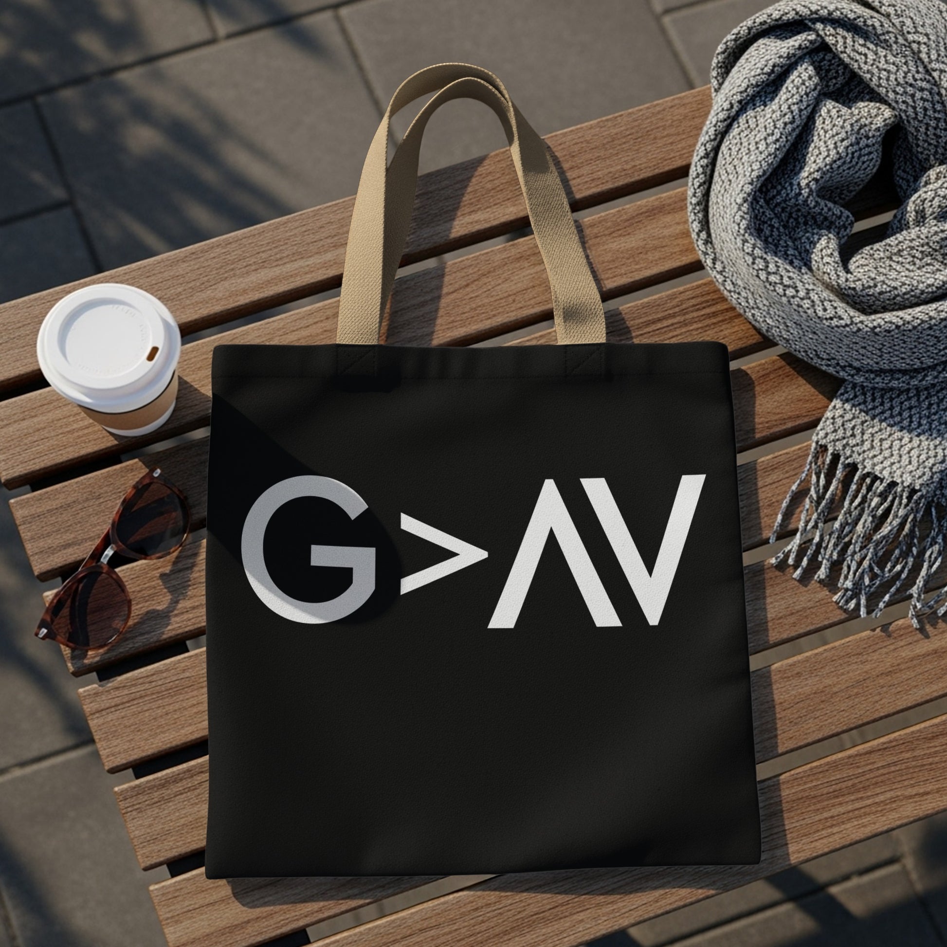 Black tote bag with white "G > AV" graphic on a wooden bench.