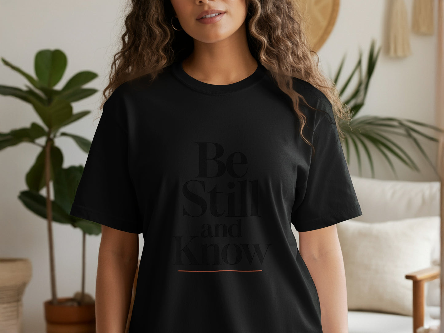 Black t-shirt with text "Be Still and Know" and an orange line above the word Know.