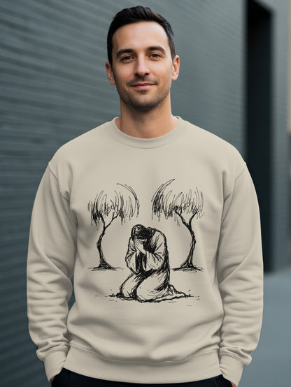Man wearing a beige sweatshirt with a sketch of Jesus kneeling between two trees.