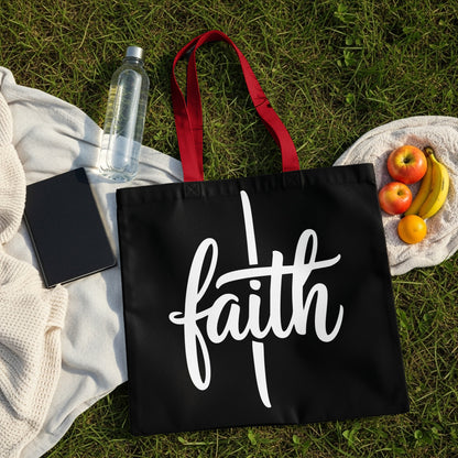 Black tote bag with white "faith" text and red handles, on grass with fruit and water.