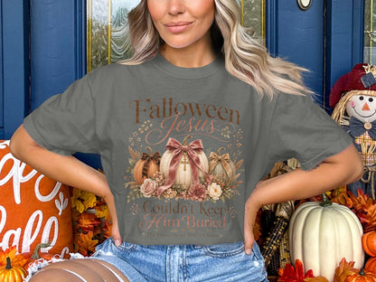 "Falloween Jesus Couldn't Keep Him Buried" text on a gray t-shirt with pumpkins and flowers.