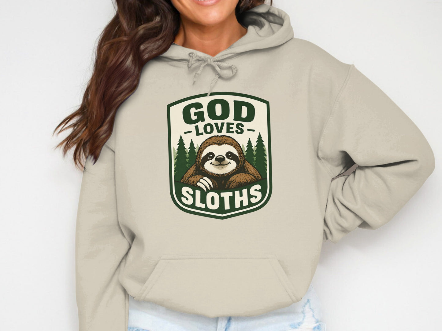 Beige hoodie with a graphic of a smiling sloth in a forest, reading "GOD LOVES SLUTHS".
