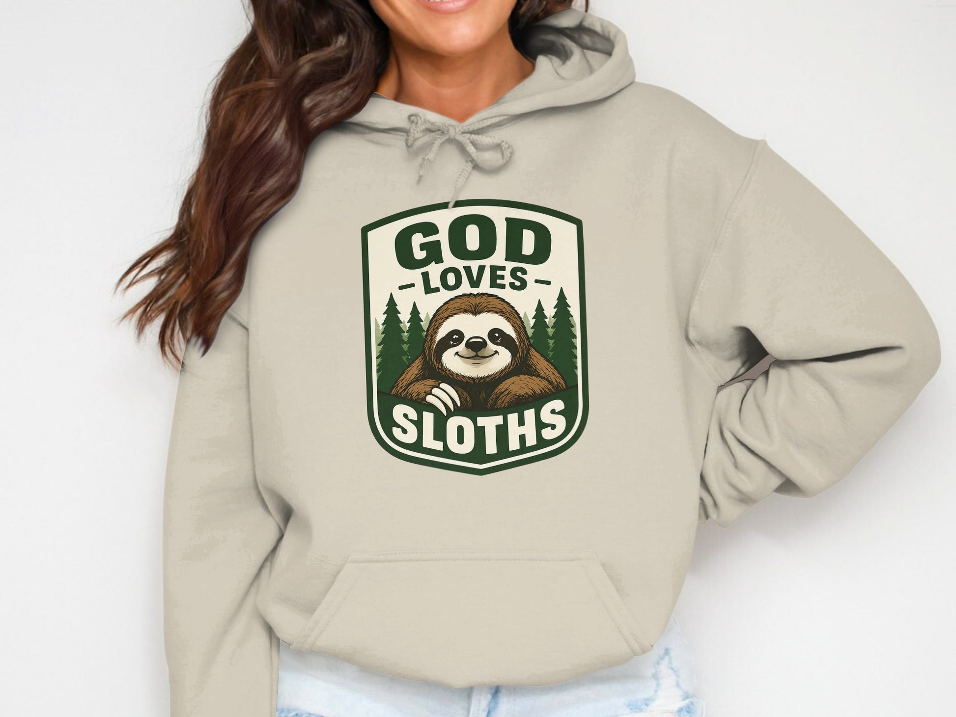 Beige hoodie with a graphic of a smiling sloth in a forest, reading "GOD LOVES SLUTHS".