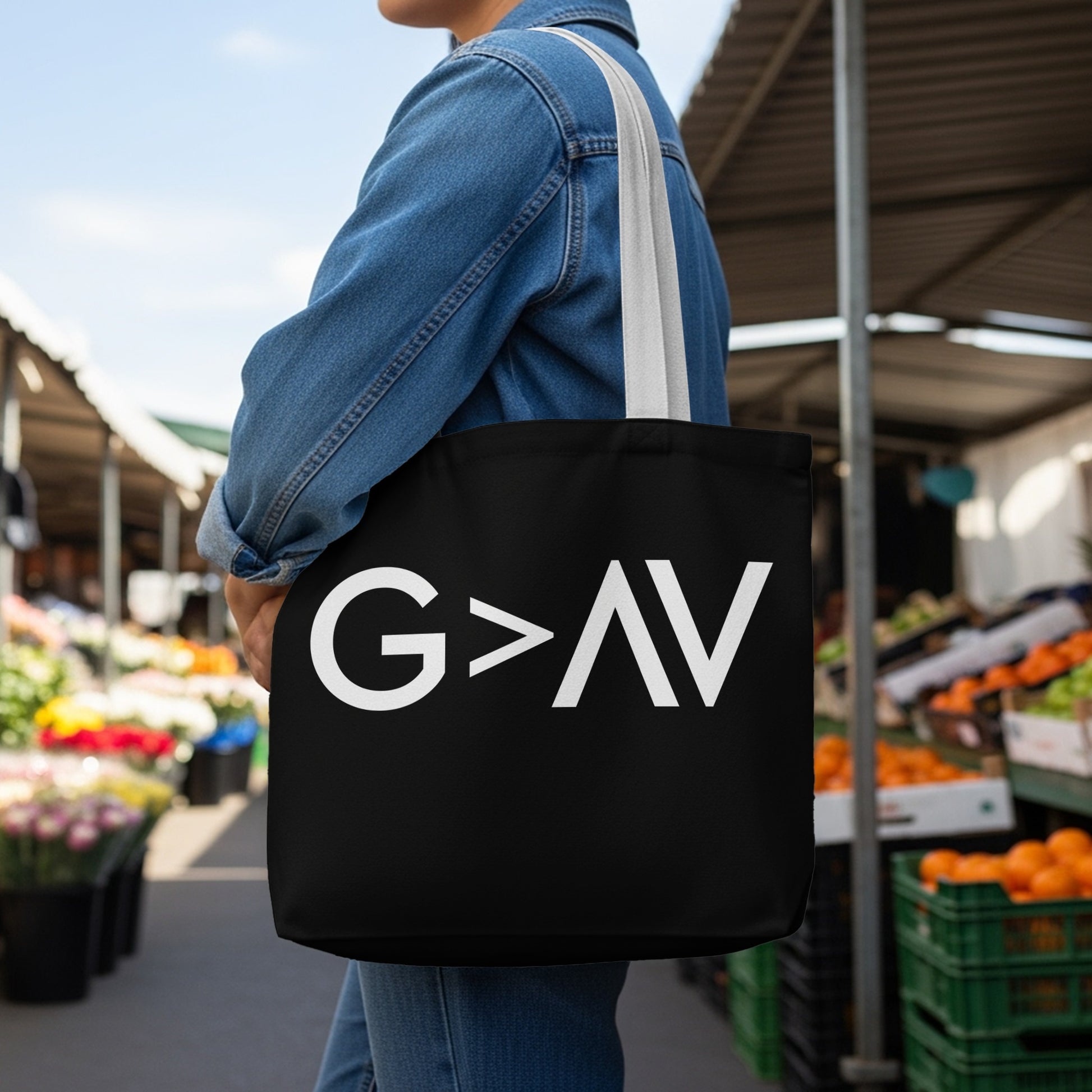 Black tote bag with white "G>AV" graphic, worn by a person at an outdoor market.