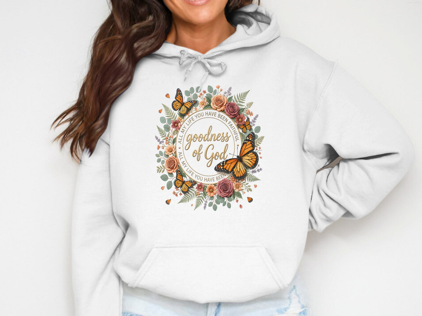 White hoodie with floral wreath and butterfly design, featuring text about God's goodness.